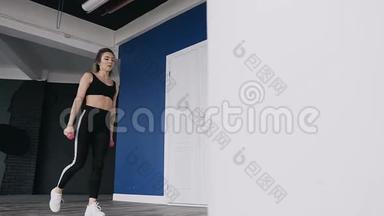 漂亮的健身金发女孩在健身房用哑铃做腿锻炼。 她穿着黑色运动服